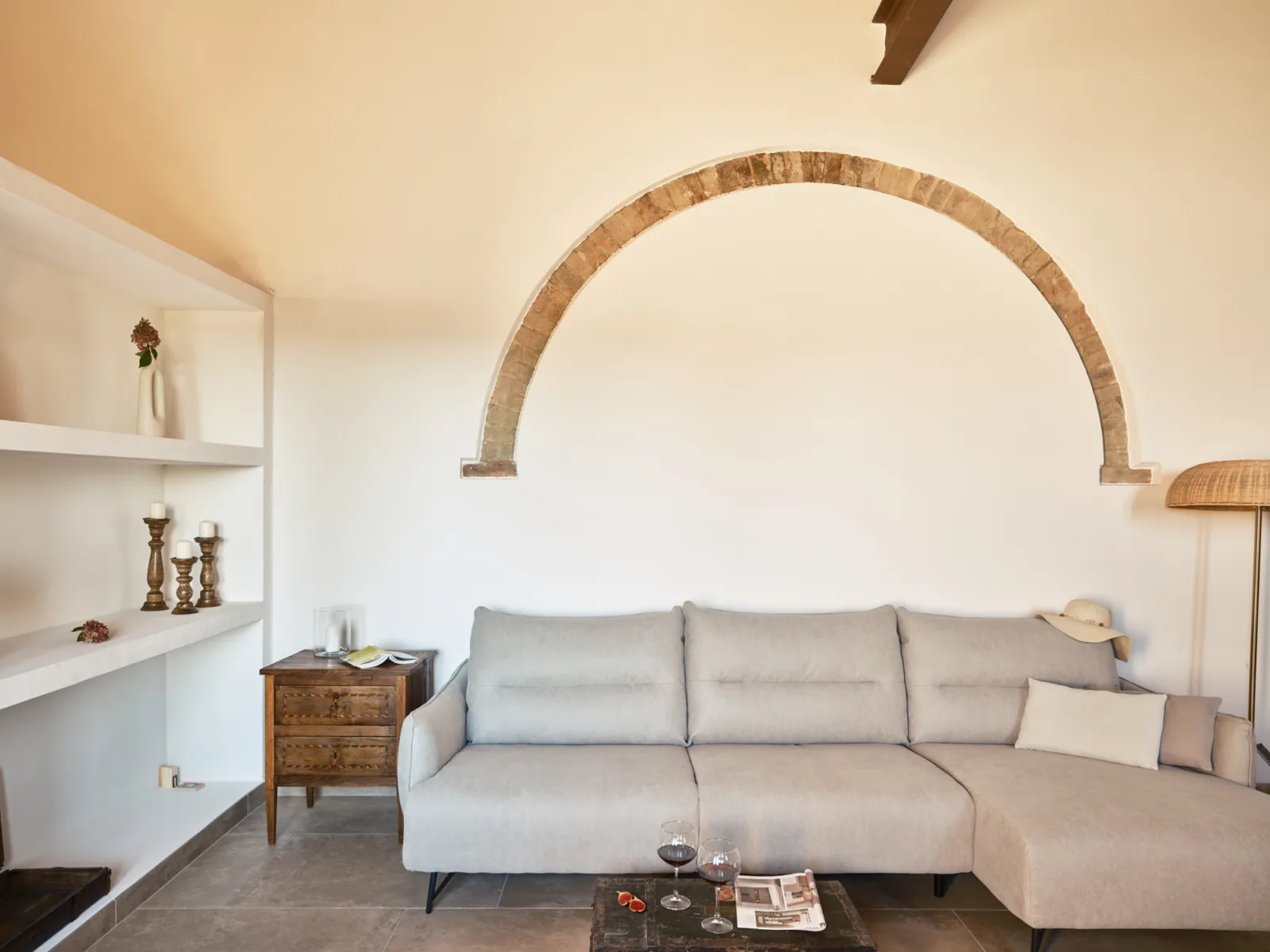 Interior of Villa Eos: a stone arch frames a sitting area with a soft grey sofa and warm ochre walls.